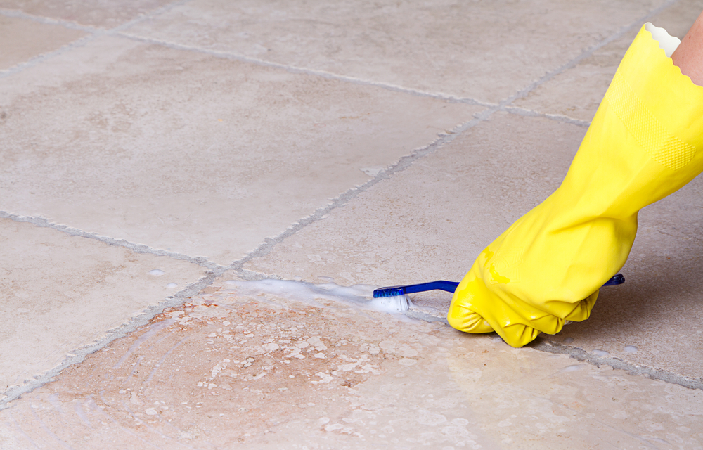 Person with a yellow glove cleaning grout with a toothbrush