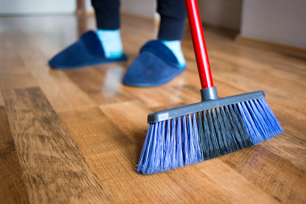 a person wearing blue house slippers sweeping a hardwood floor with a broom