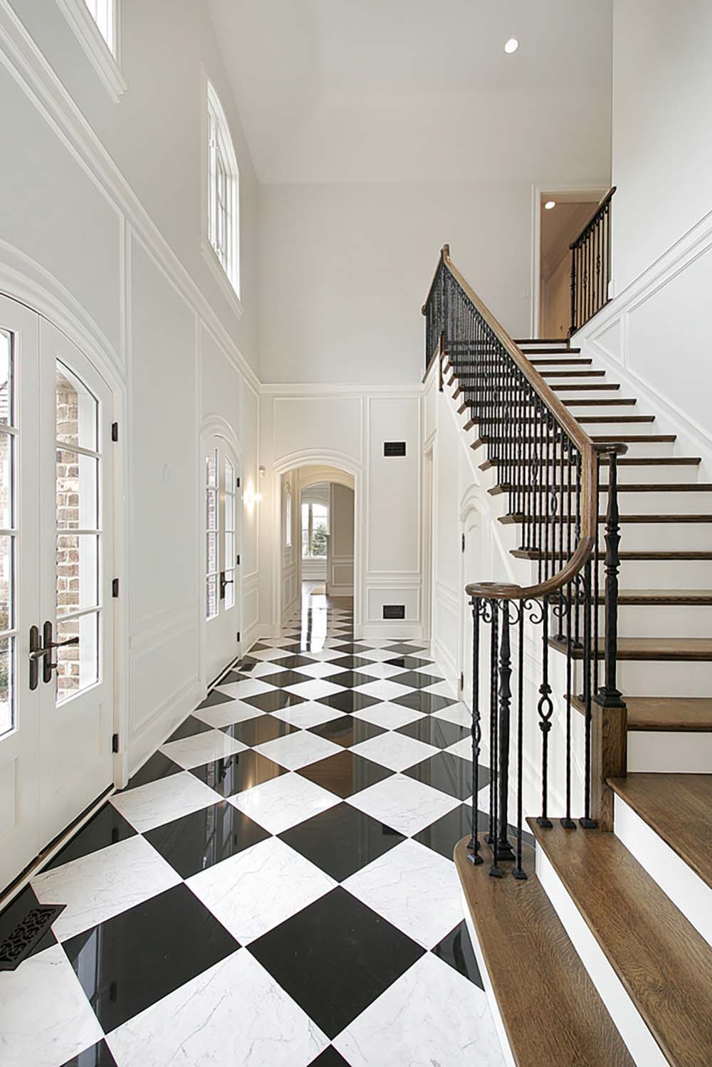 A foyer with white walls and a grand staircase with black and white checkerboard floors.