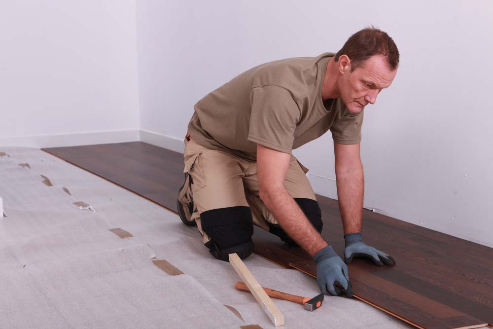 A man lays dark brown laminate flooring.
