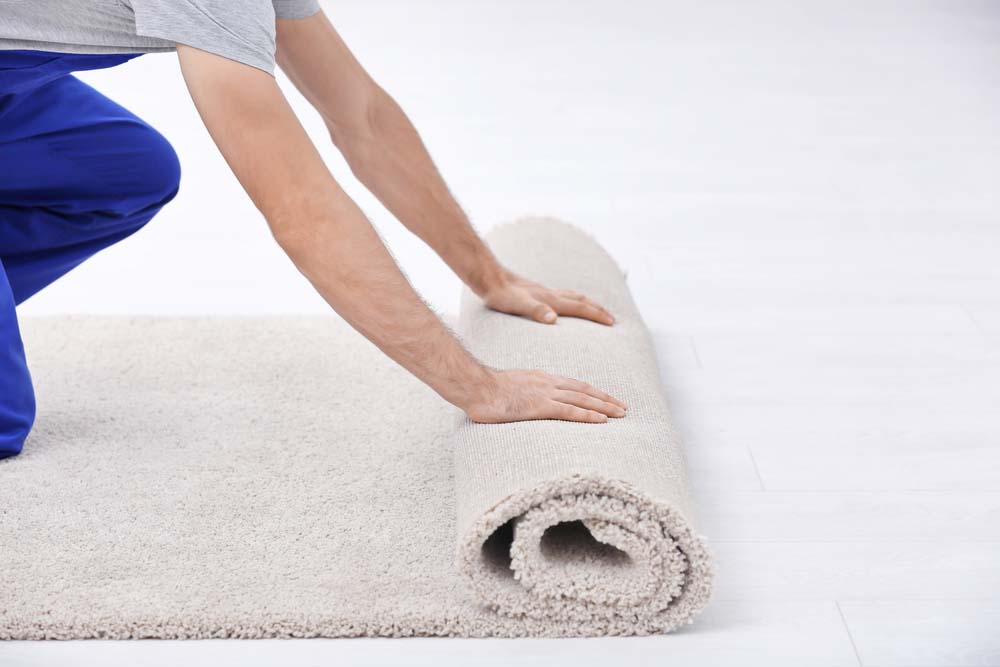 A man unrolls carpeting to install it on a floor. 