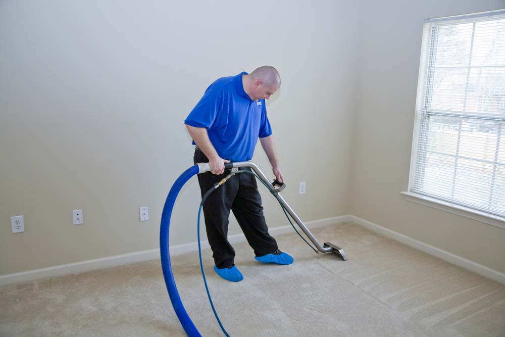 A man uses a steam cleaner on a beige carpet.