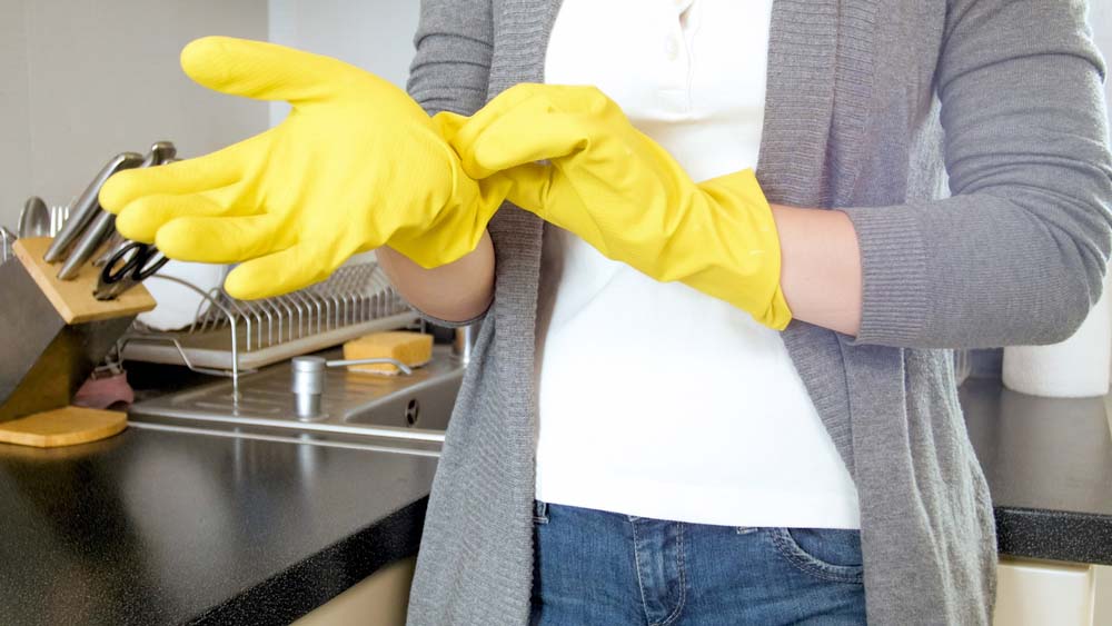 A woman puts on yellow rubber gloves.