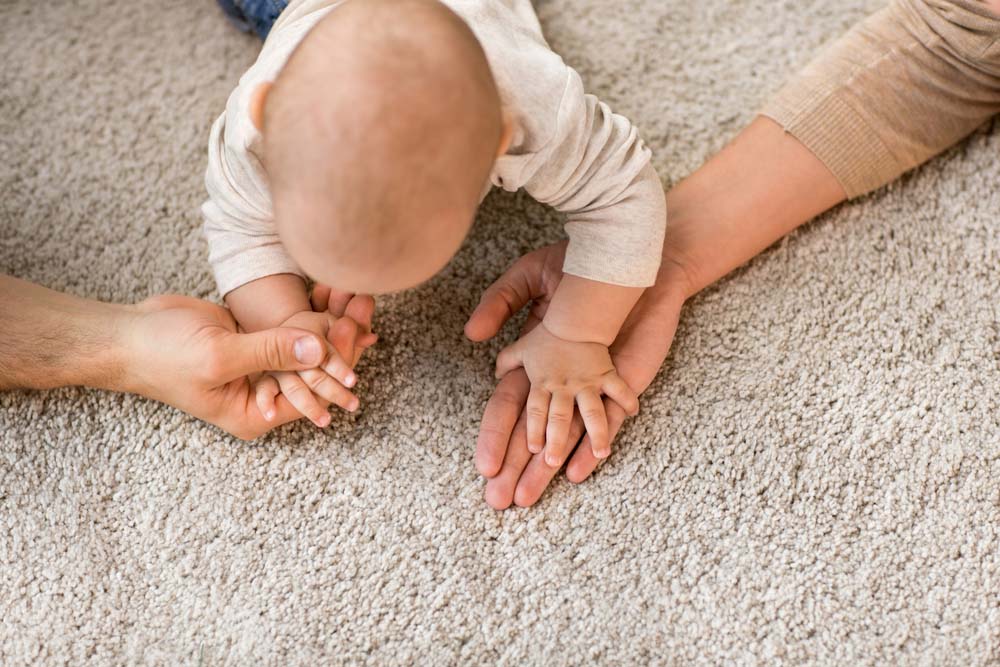 Baby on knees on the carpet holding parents hands.