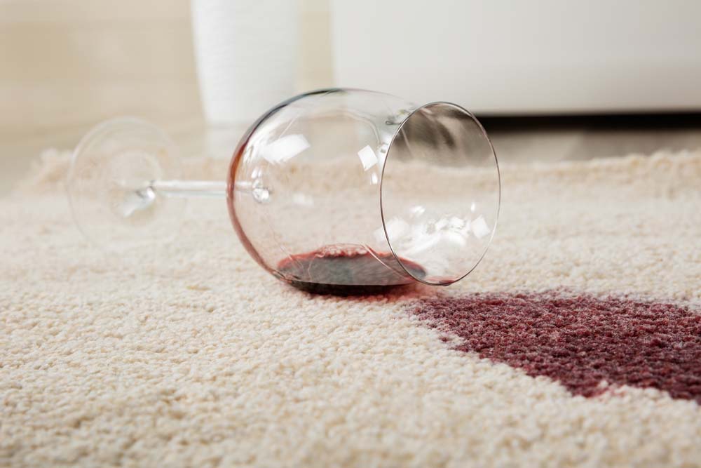 Glass of red wine spilled on a beige carpet.